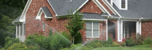 A red brick house with a manicured lawn and working sprinkler system, surrounded by trees.